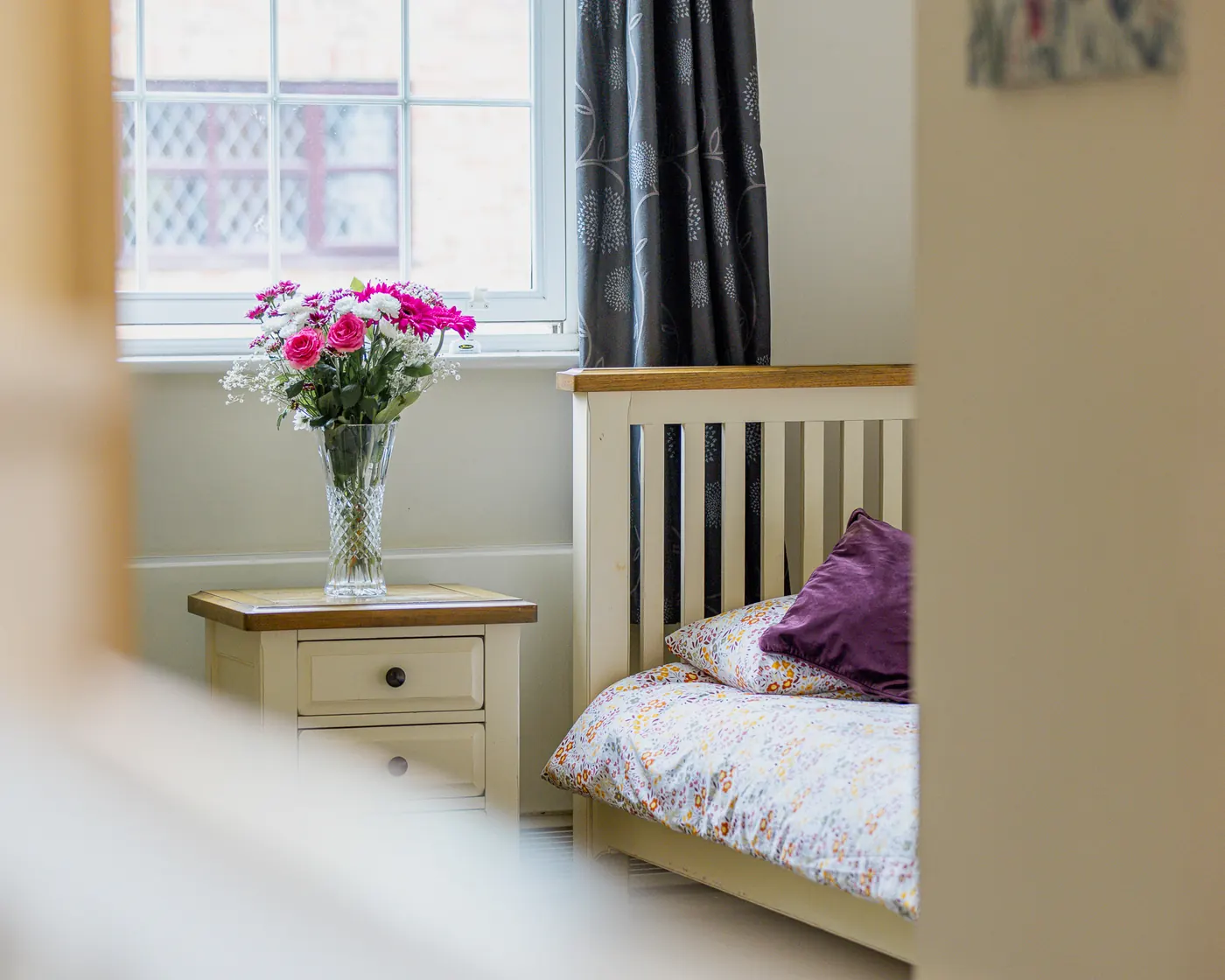 Bedroom with a single bed and a vase of pink flowers on the bedside cabinet