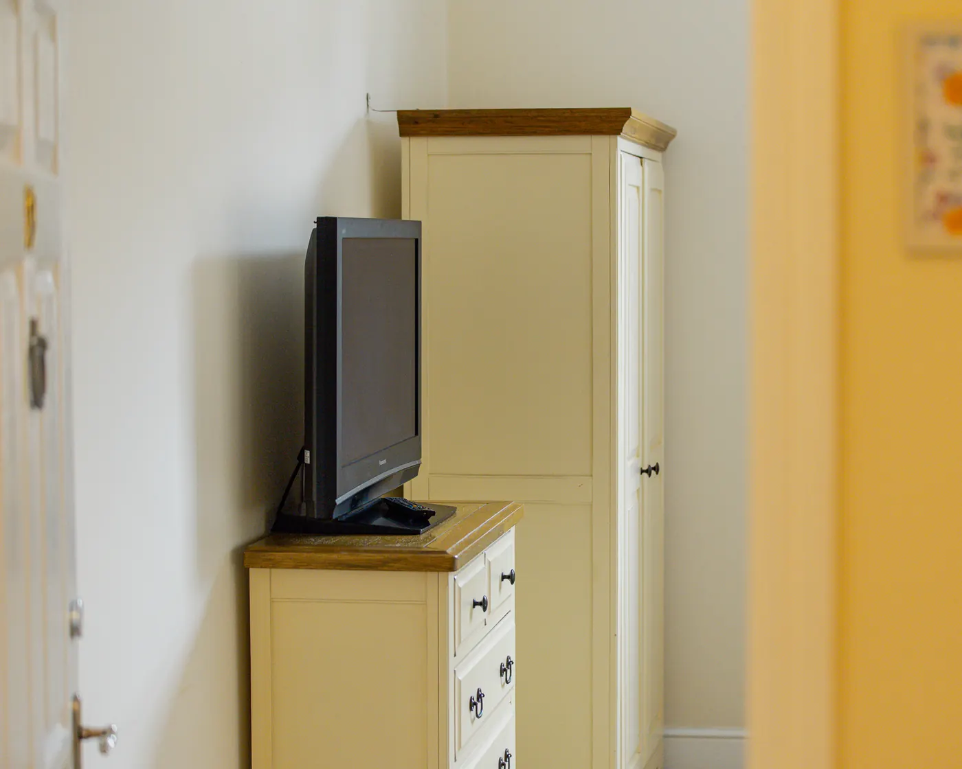 Corner of a bedroom with a television on a chest of drawers and a wardrobe